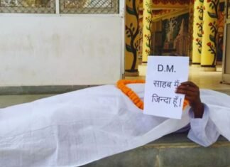 DM साहब मैं जिंदा हूँ…बस्ती में कफन ओढ़कर डीएम ऑफिस के बाहर लेट गया बुजुर्ग, मचा बवाल